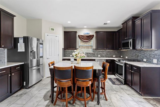 Modern kitchen with dark wood cabinets, stainless steel appliances, and a central island with seating. | Image 11