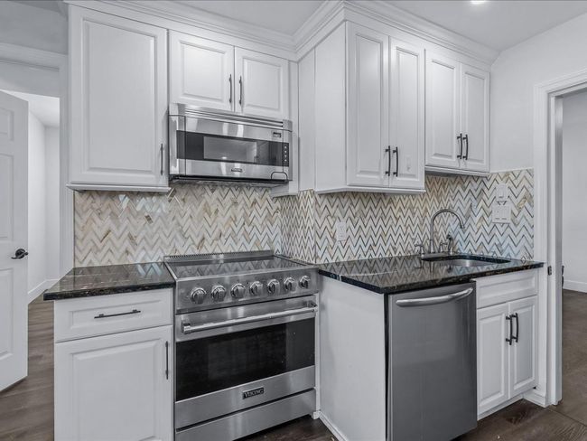 Kitchen with appliances with stainless steel finishes, white cabinets, a sink, dark stone counters, and dark wood finished floors | Image 7
