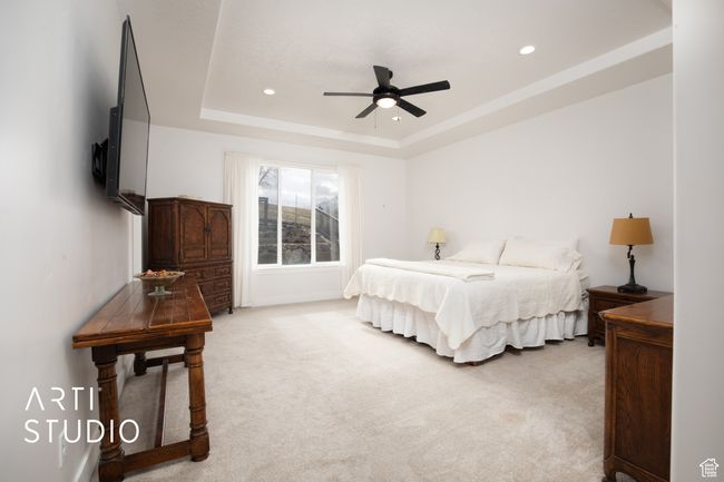 Bedroom featuring ceiling fan, light colored carpet, and a tray ceiling | Image 19