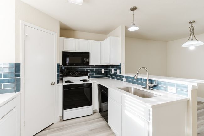 Kitchen featuring light wood-style flooring, a peninsula, a sink, black appliances, and backsplash | Image 8