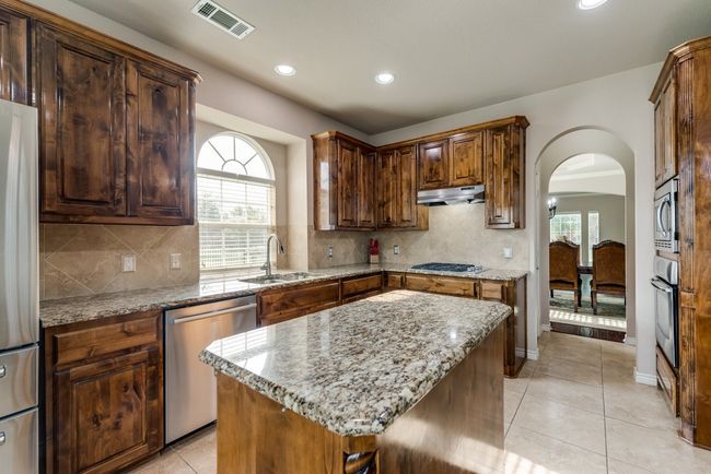 Kitchen with appliances with stainless steel finishes, a sink, arched walkways, under cabinet range hood, and light stone counters | Image 10