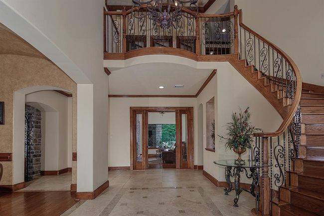 Impressive foyer with elegant flooring and a beautiful, curved wooden staircase with intricate iron work. The space is enhanced by soaring ceilings and a striking chandelier. | Image 5