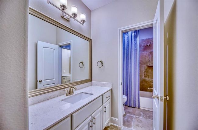 This bathroom features a sleek design with a marble countertop vanity, modern lighting, and a large mirror. It includes a shower-tub combo with tile surround, accented by a blue-striped curtain, and has neutral tones throughout. | Image 42