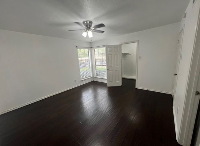 Unfurnished bedroom featuring dark wood-type flooring, a spacious closet, a ceiling fan, and baseboards | Image 15