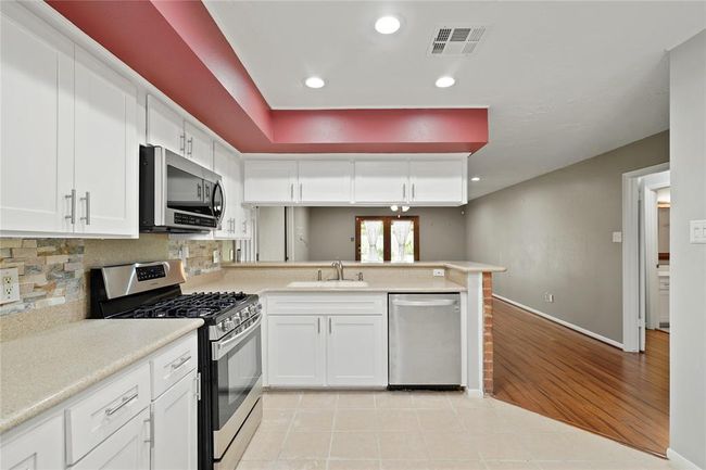 Modern kitchen with white cabinets and stainless steel appliances. Features a spacious layout with recessed lighting, and an open view to the living area. | Image 12
