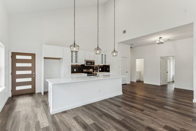 Kitchen featuring a high ceiling, appliances with stainless steel finishes, glass insert cabinets, a large island, and white cabinetry | Image 17