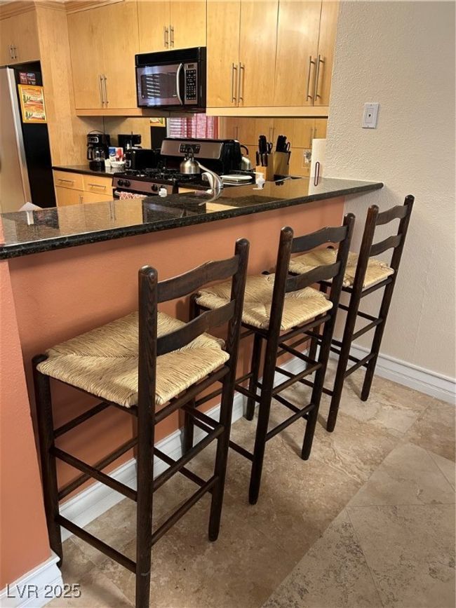 Kitchen with refrigerator, stove, a breakfast bar area, a peninsula, and a textured wall | Image 24