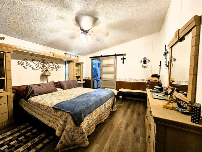 Bedroom featuring a textured ceiling, dark wood-style floors, a barn door, wainscoting, and a ceiling fan | Image 9