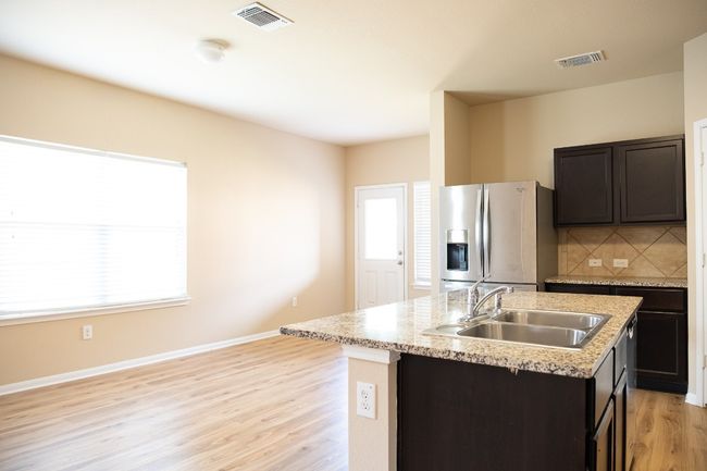 Kitchen with stainless steel fridge with ice dispenser, a sink, a center island with sink, tasteful backsplash, and light wood-style floors | Image 9