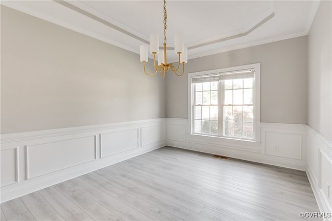 Formal dining room with tray ceiling, ornamental molding, wainscoting, chandelier, and light wood-style floors | Image 7