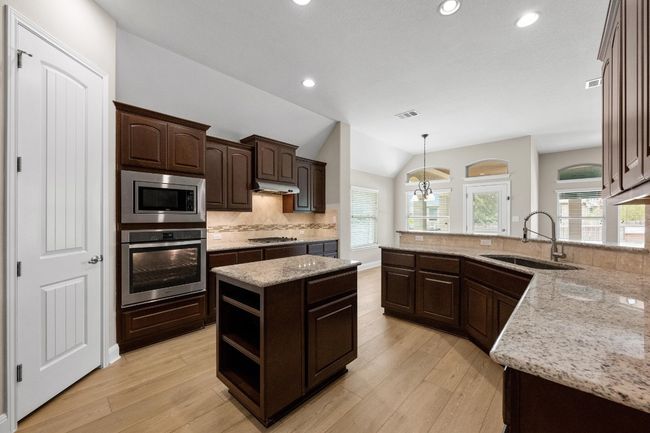 Kitchen with stainless steel appliances, dark brown cabinetry, tasteful backsplash, light wood-type flooring, and light stone counters | Image 9