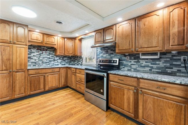 Kitchen with stone countertops, brown cabinets, stainless steel electric stove, and under cabinet range hood | Image 12