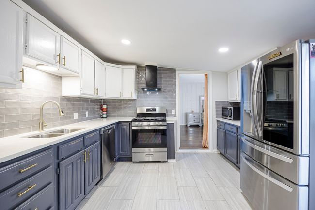 Kitchen featuring light countertops, appliances with stainless steel finishes, a sink, and wall chimney exhaust hood | Image 10