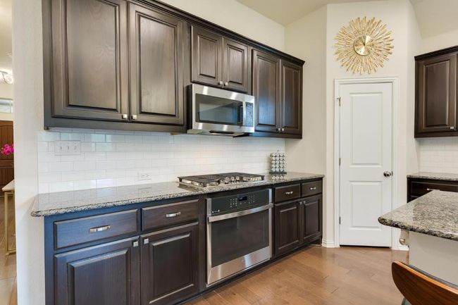 Kitchen with appliances with stainless steel finishes, dark brown cabinets, backsplash, and wood finished floors | Image 8