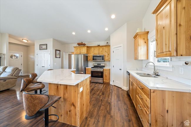 Kitchen featuring stainless steel appliances, a center island, dark wood-style floors, a sink, and a kitchen bar | Image 16