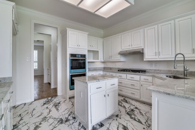 Kitchen with a sink, double oven, stainless steel gas stovetop, light marble finish floors, and under cabinet range hood | Image 9