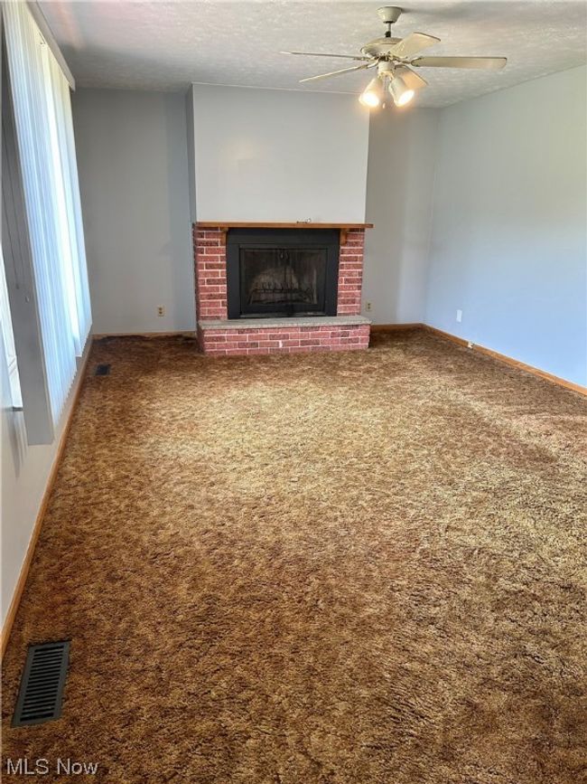 Unfurnished living room with ceiling fan, a brick fireplace, dark colored carpet, and a textured ceiling | Image 5