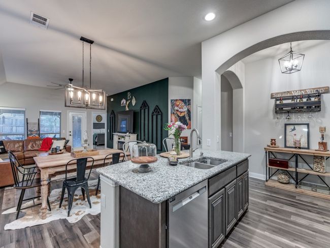 Kitchen featuring decorative light fixtures, dishwasher, an island with sink, sink, and light stone counters | Image 7
