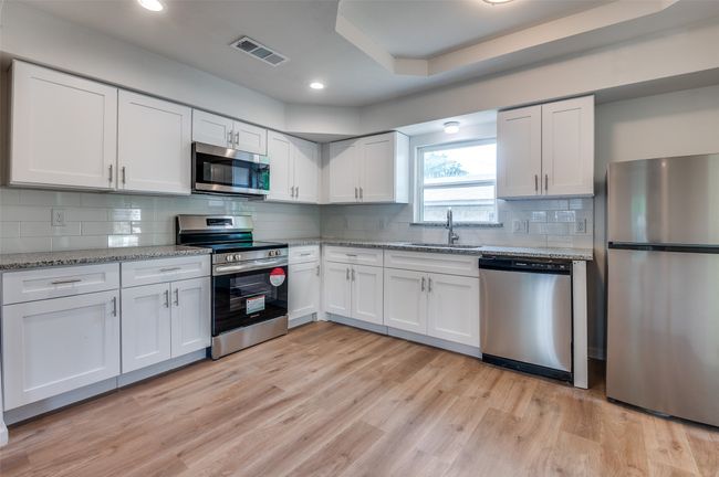 Kitchen featuring a sink, light wood-style flooring, white cabinets, appliances with stainless steel finishes, and visible vents | Image 10