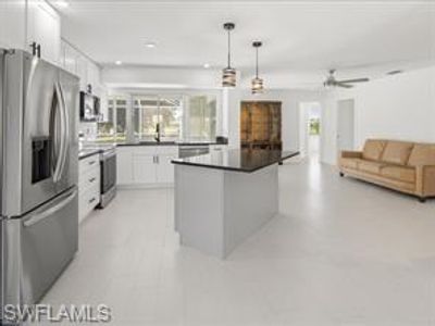 Kitchen featuring decorative light fixtures, white cabinetry, stainless steel fridge with ice dispenser, and plenty of natural light | Image 3