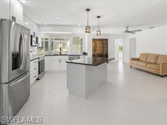 Kitchen featuring decorative light fixtures, white cabinetry, stainless steel fridge with ice dispenser, and plenty of natural light | Image 3