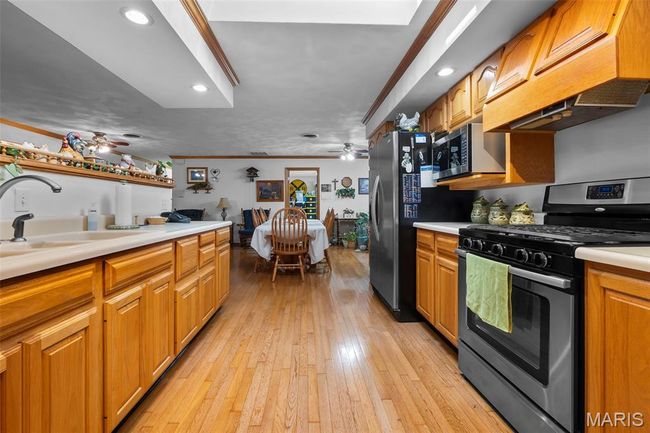 Kitchen featuring stainless steel appliances, a ceiling fan, ventilation hood, light countertops, and ornamental molding | Image 68