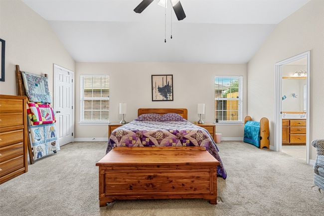 Bedroom with lofted ceiling, carpet floors, baseboards, connected bathroom, and a ceiling fan | Image 19