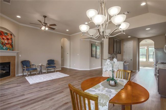 Dining area featuring arched walkways, ceiling fan, light wood-style flooring, a tiled fireplace, and a chandelier | Image 10