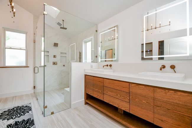 Sleek lines continue to define your primary ensuite bath, with rich honey colored cabinetry, below dual sinks and fun individual mirrors, above. The huge glass enclosed, rimless shower is sure to deliver peaceful vibes. | Image 27