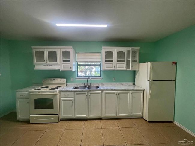 Kitchen featuring a sink, under cabinet range hood, white appliances, white cabinets, and light countertops | Image 4
