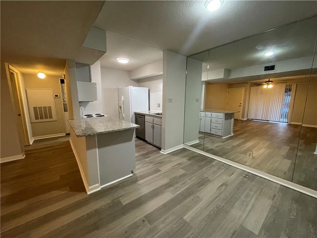 Kitchen featuring white refrigerator with ice dispenser, kitchen peninsula, stainless steel dishwasher, a textured ceiling, and wood-type flooring | Image 4