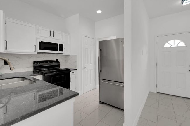 Kitchen featuring dark stone counters, freestanding refrigerator, black / electric stove, white cabinets, and white microwave | Image 5