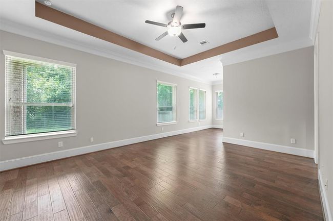 This primary suite is huge—you’ve got room for a king bed plus a cozy sitting area under that elegant tray ceiling. Rich hardwood floors and three big windows bring in tons of light and frame those peaceful backyard views. It’s the perfect retreat for morning coffee or curling up with a book. | Image 13