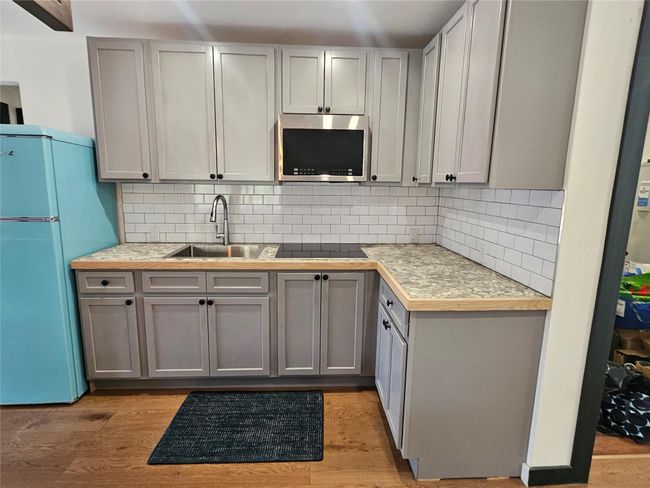 Kitchen view of stainless steel microwave, a sink, black electric stovetop, and decorative backsplash | Image 16