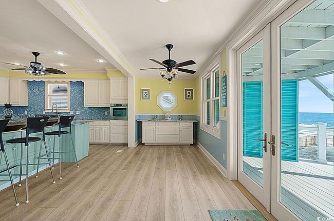 Kitchen featuring light wood finished floors, white cabinets, ornamental molding, a kitchen bar, and stainless steel oven | Image 12