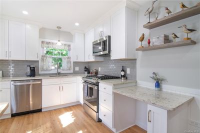 Kitchen featuring sink, light wood-type flooring, hanging light fixtures, stainless steel appliances, and white cabinets | Image 2