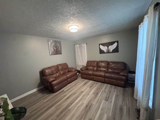 Living area with wood finished floors, a textured ceiling, and baseboards | Image 8