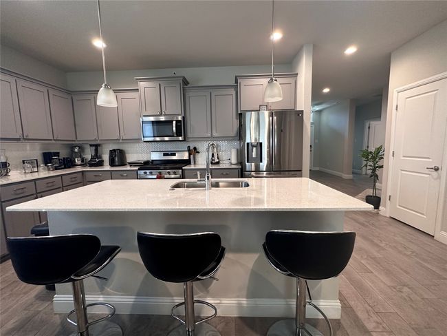Kitchen featuring gray cabinetry, appliances with stainless steel finishes, light wood-type flooring, a kitchen bar, and tasteful backsplash | Image 5