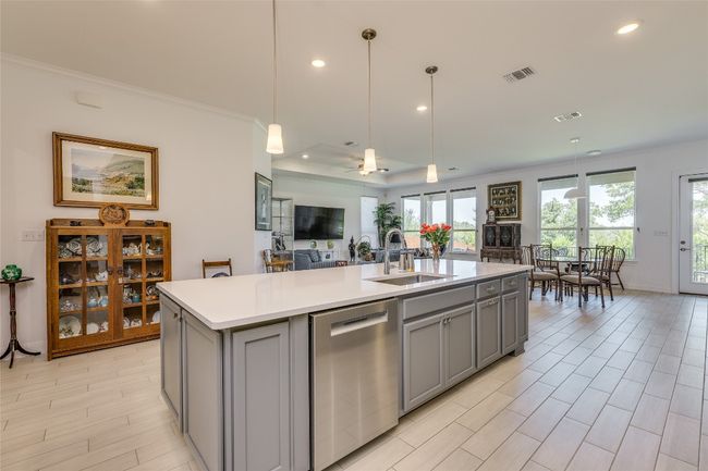 Kitchen featuring crown molding, stainless steel dishwasher, pendant lighting, open floor plan, and a kitchen island with sink | Image 8