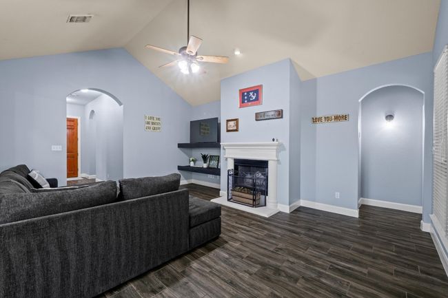 Living room featuring ceiling fan, arched walkways, a fireplace with raised hearth, and dark wood-style flooring | Image 10