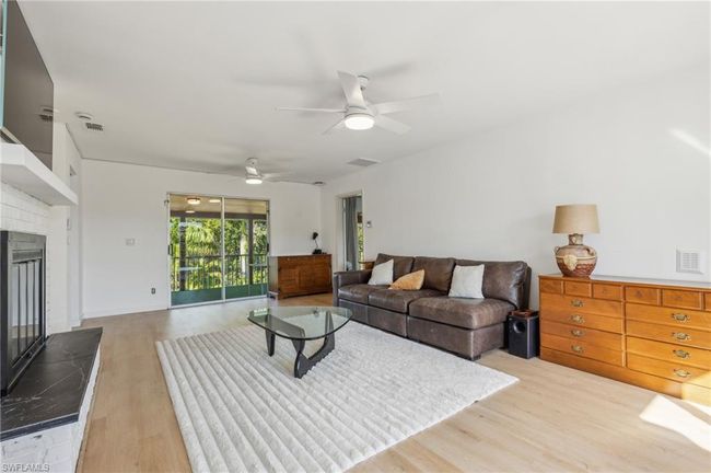 Living room with a brick fireplace, a ceiling fan, light wood-style flooring, and visible vents | Image 19