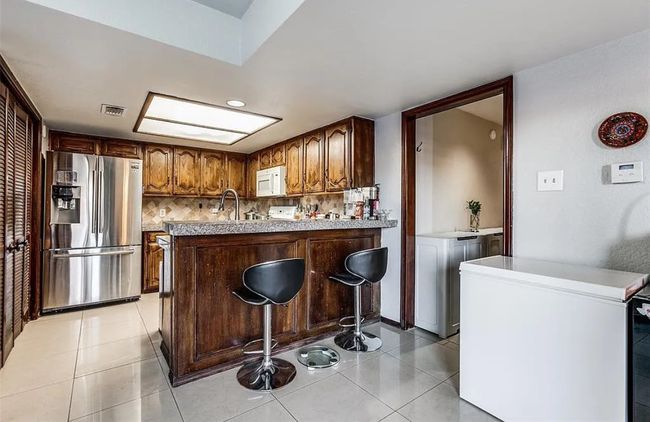 Kitchen with stainless steel fridge with ice dispenser, white microwave, a peninsula, light tile patterned floors, and light countertops | Image 5
