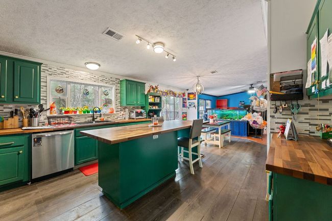 Kitchen with butcher block counters, green cabinets, stainless steel dishwasher, a sink, and a textured ceiling | Image 8