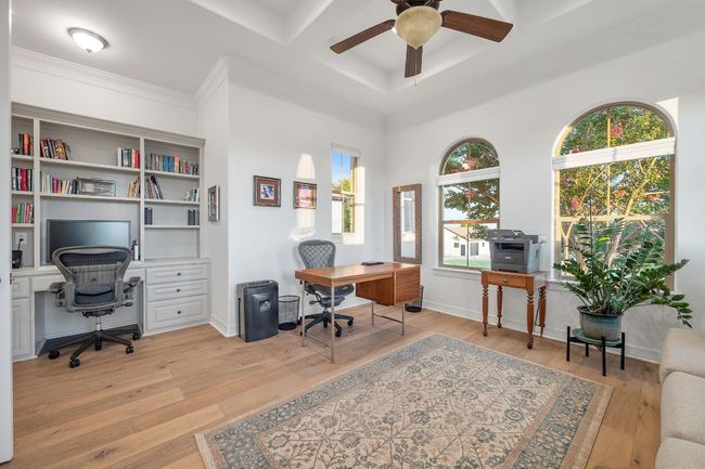 Home office with a ceiling fan, plenty of natural light, light wood-type flooring, crown molding, and coffered ceiling | Image 22