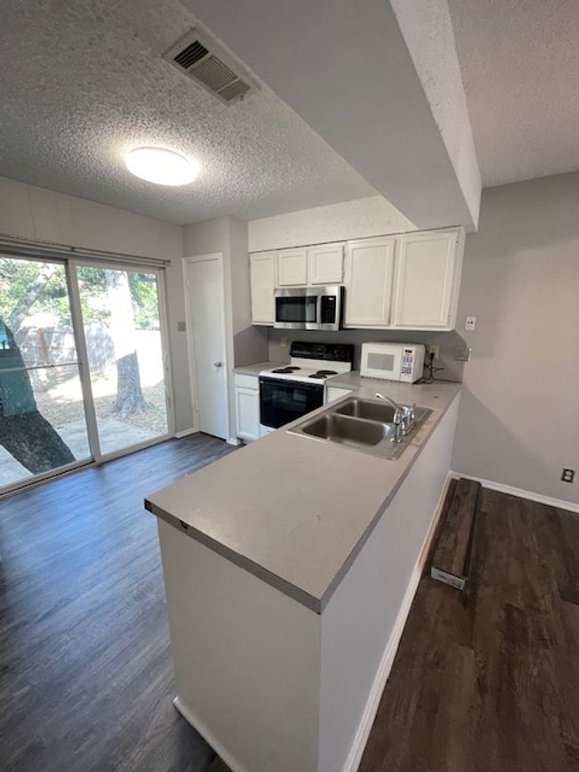 Kitchen featuring electric range, a textured ceiling, white cabinets, dark wood-type flooring, and a peninsula | Image 4
