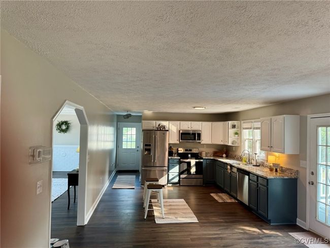Kitchen with stainless steel appliances, a textured ceiling, dark wood-style flooring, white cabinetry, and plenty of natural light | Image 7