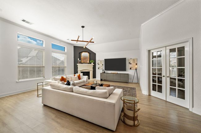 Explore a light-filled living room with expansive windows that illuminate the space. Featuring designer lighting fixtures, a cozy fireplace, and patio access, this room’s layout invites both entertaining and relaxation. The open design seamlessly integrates a home office area, blending functionality with style. | Image 12