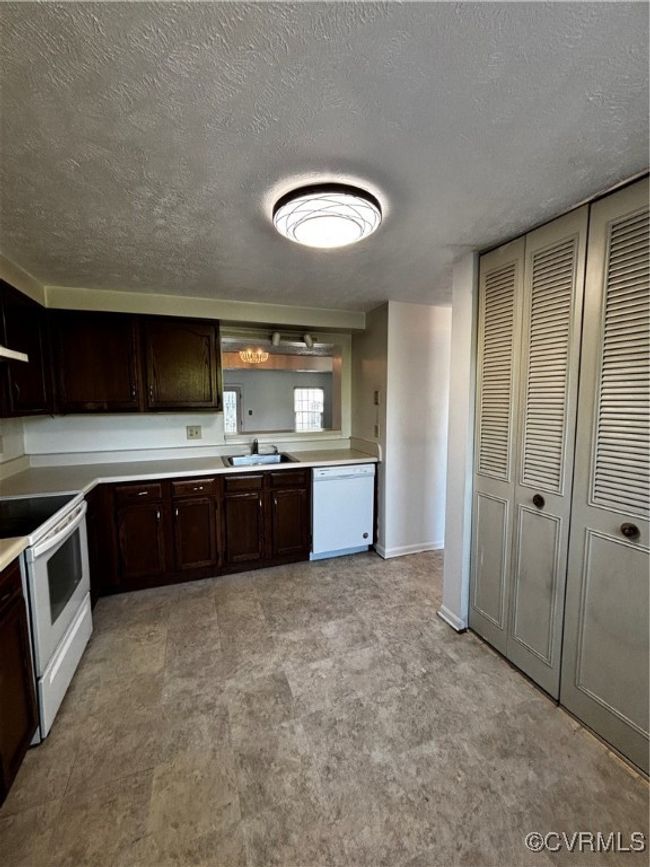 Kitchen with dishwashing machine, stove, dark brown cabinets, a textured ceiling, and light countertops | Image 5