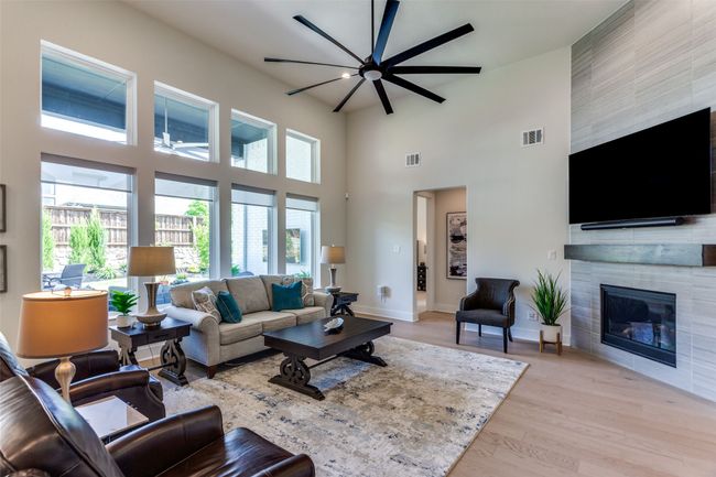 Living area featuring a high ceiling, healthy amount of natural light, a tiled fireplace, light wood-style floors, and a ceiling fan | Image 10