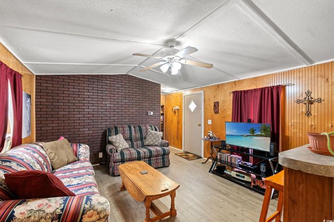 Living room with wood finished floors, ceiling fan, lofted ceiling, wooden walls, and a textured ceiling | Image 6